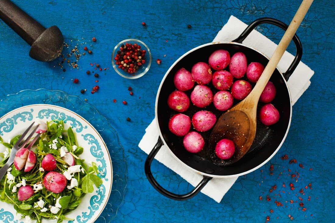 Caramelised radishes in a pan with a plate of feta and peas