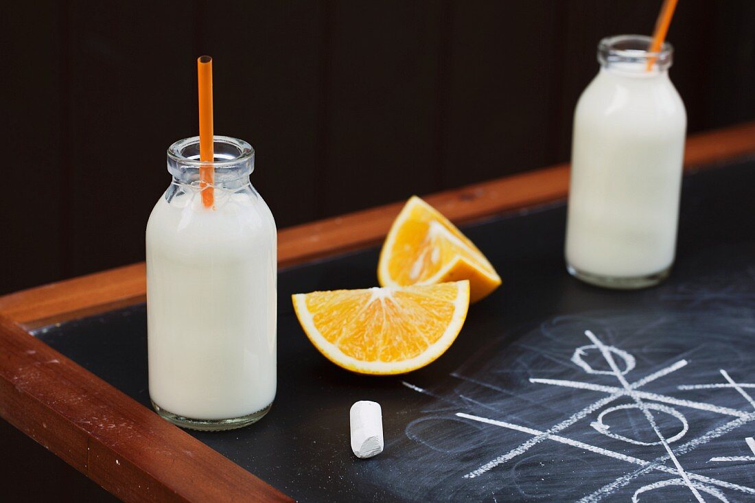 Mini-Milchflaschen und Orangenschnitze auf einer Kreidetafel