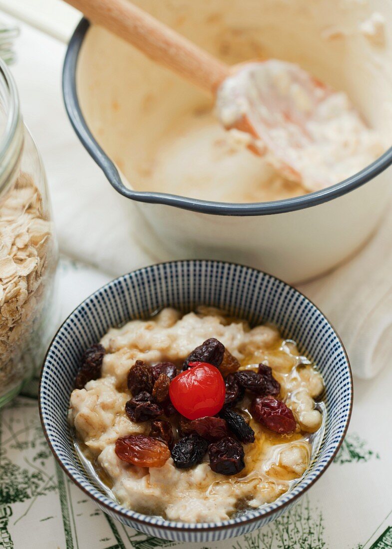 A bowl of porridge served with dried fruits, honey and a cocktail cherry