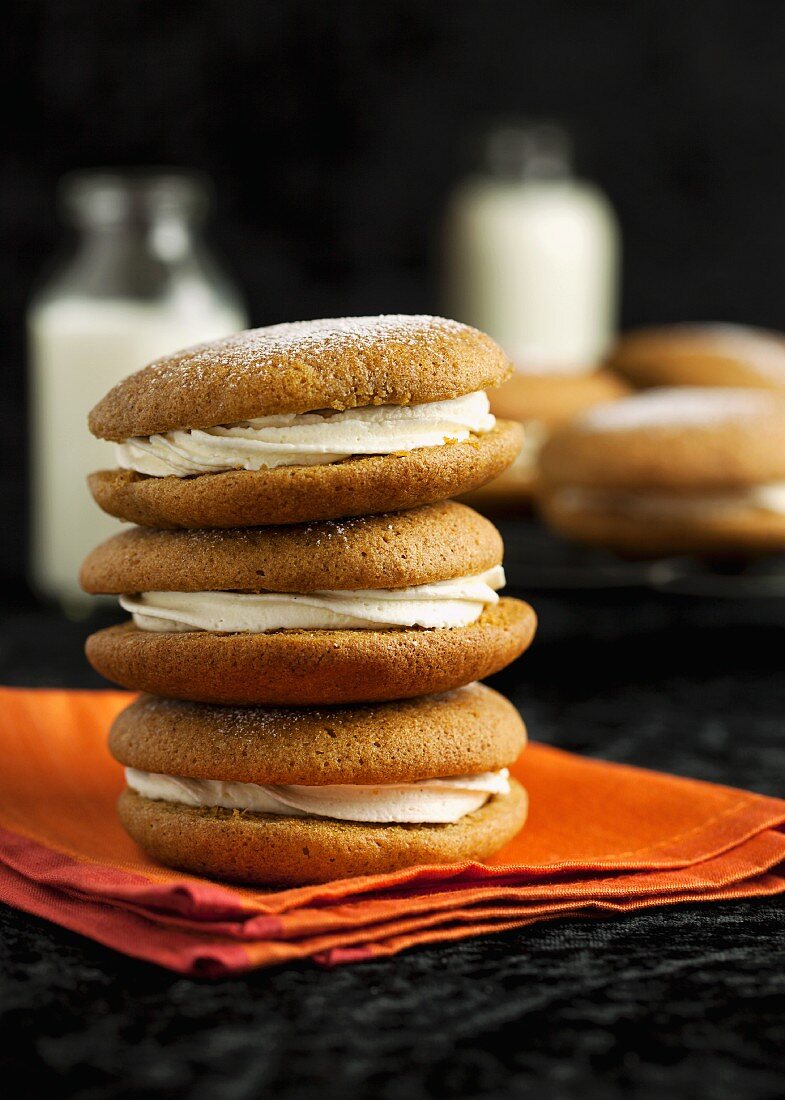 Pumpkin and ginger whoopie pies stacked on an orange napkin and dusted with icing sugar (USA)