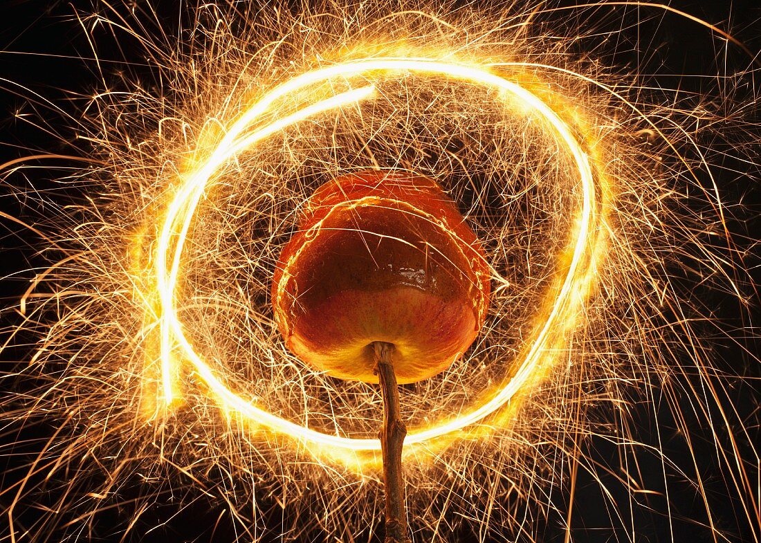Karamellapfel auf Zweig in einem Lichtkreis von einer Wunderkerze
