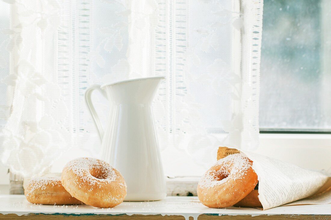 Zucker-Donuts mit weißem Krug auf altem Fensterbrett