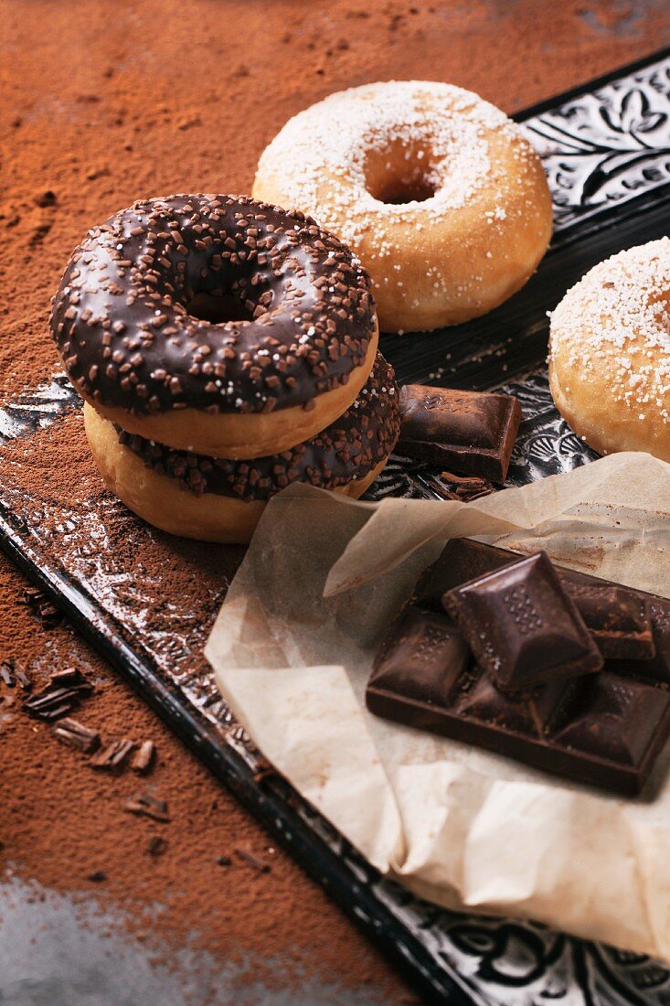 Chocolate glazed doughnuts, sugared doughnuts and dark chocolate on a tray