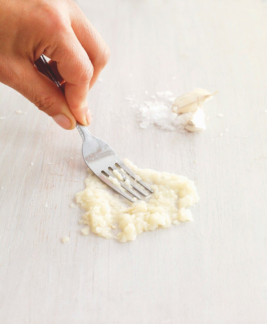 Garlic cloves being crushed with a fork