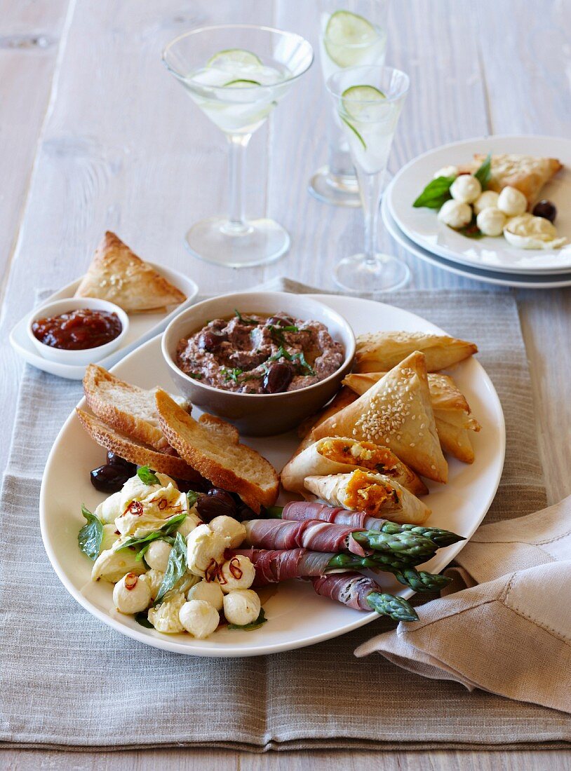 An appetizer platter with pasties, asparagus, mozarellla and a dip