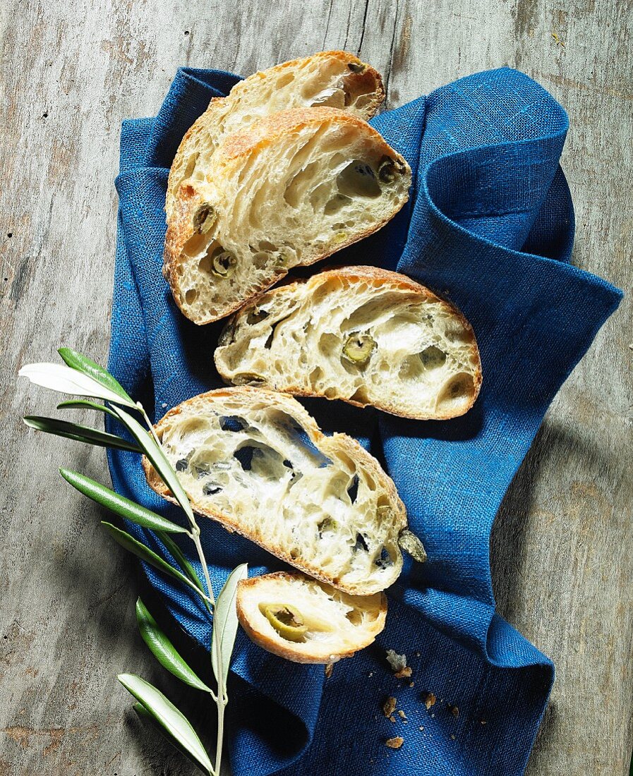Slices of olive ciabatta on a cloth with an olive sprig