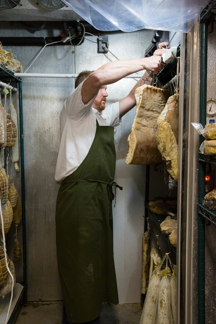 A butcher hanging sides of bacon in a refrigerated room