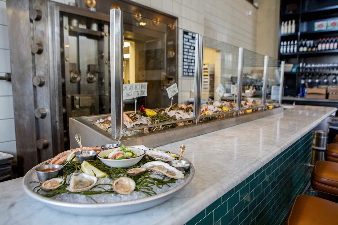 A fish restaurant with a marble bar and a display case with a tray of fresh mussels on the bar