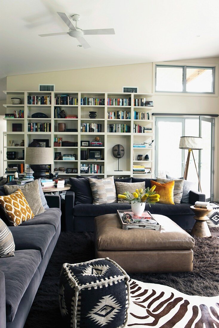 African occasional furniture, zebra-skin rug, grey sofa set with scatter cushions and ottoman in front of white shelving