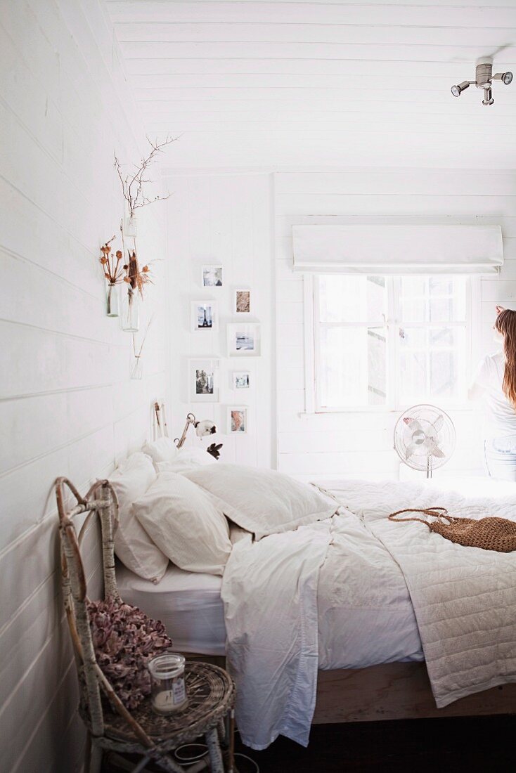 Rustic chair made from birch branches next to double bed with white bed linen in white, wood-clad bedroom