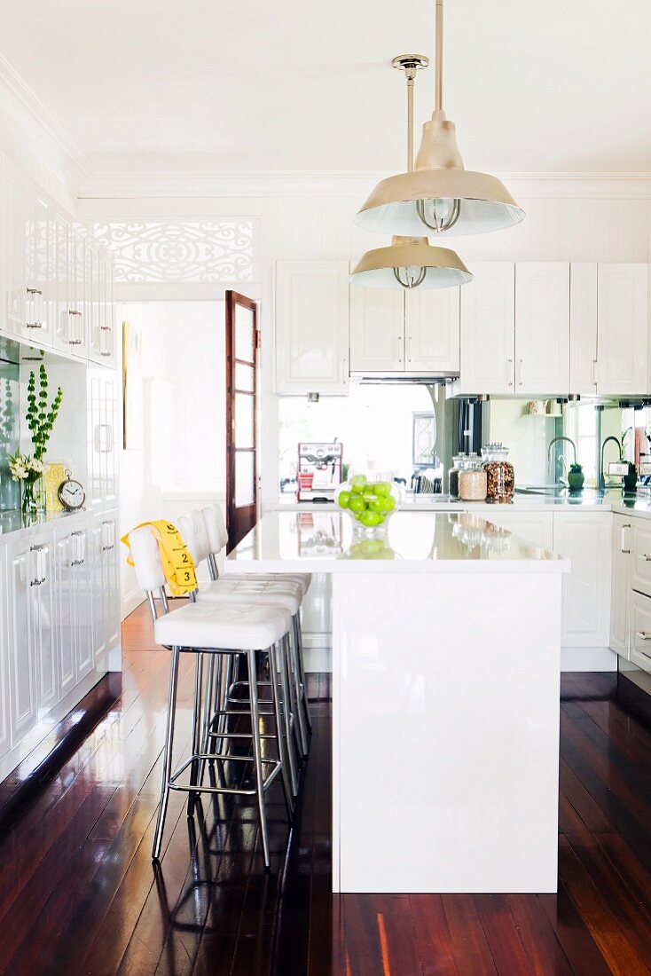 weiße Einbauküche im Landhausstil mit Küchentheke, Barhockern und glänzendem Dielenboden