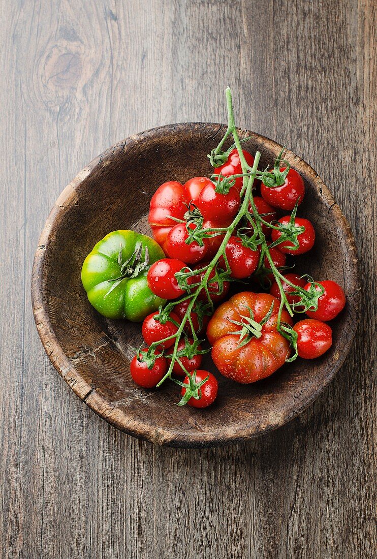 Various freshly washed tomatoes in a wooden bowl