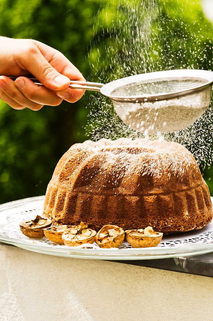 Nussgugelhupf mit Puderzucker bestreuen