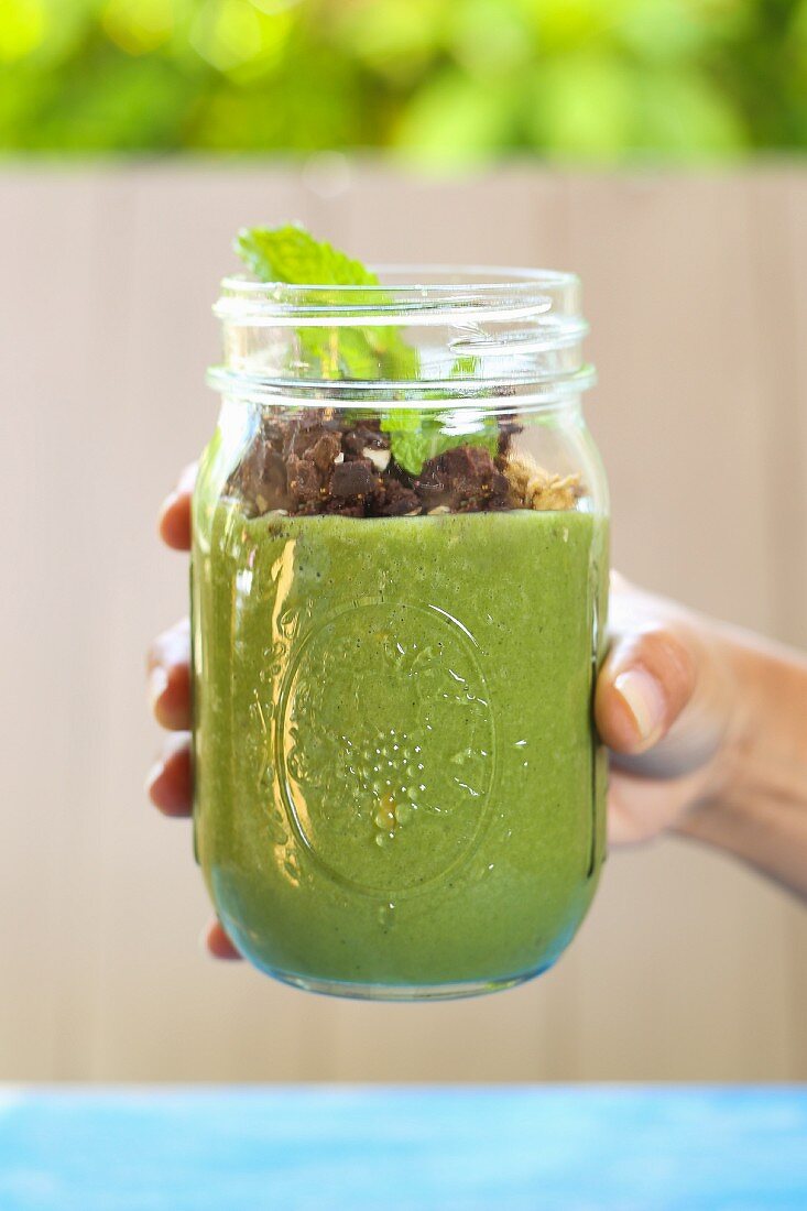 A hand holding a jar of breakfast parfait with pumpkin seed milk and cocoa nibs