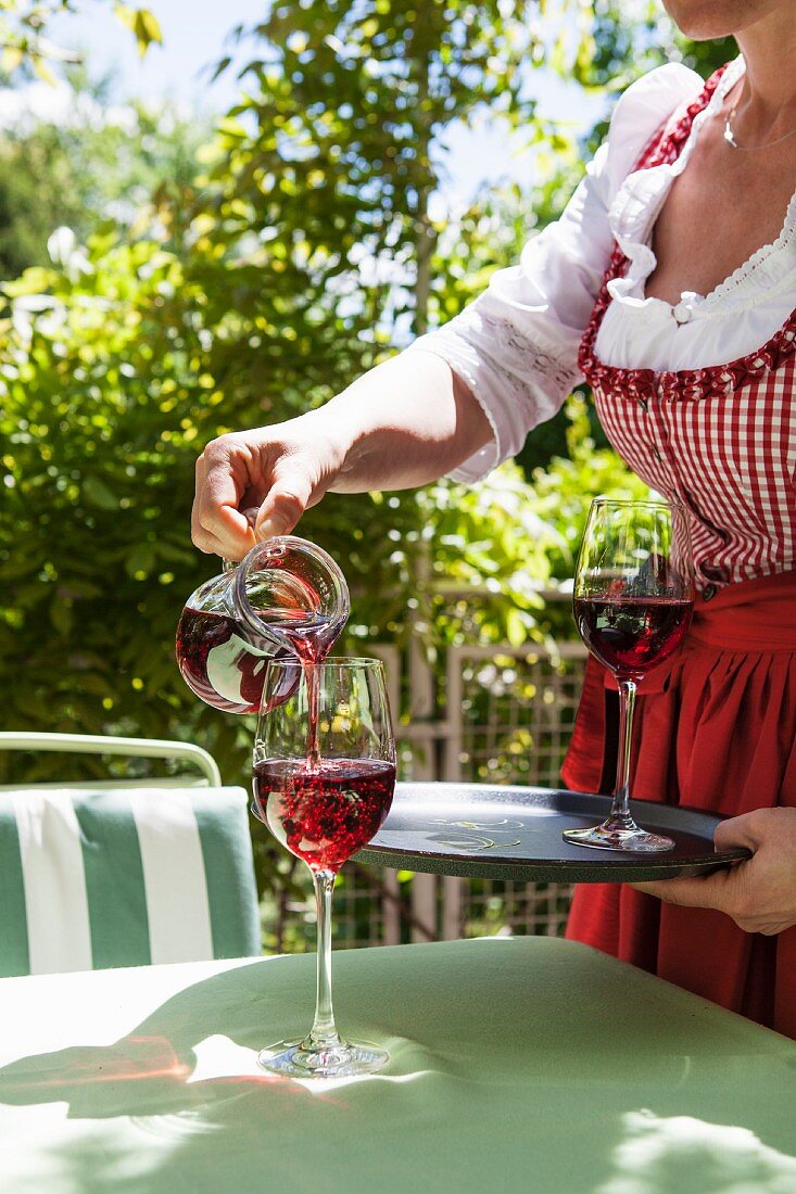 Frau giesst Rotwein in ein Glas am Gartentisch