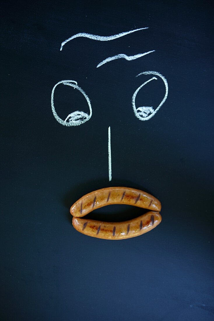 A face drawn with chalk with two sausages as a mouth