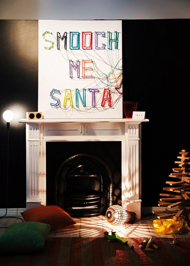 Weihnachtsdeko im Kaminzimmer: selbstgemachtes Wandbild mit Buchstaben aus bunten Wollfäden, originelle Bodenlampe und Christbaum aus Holz