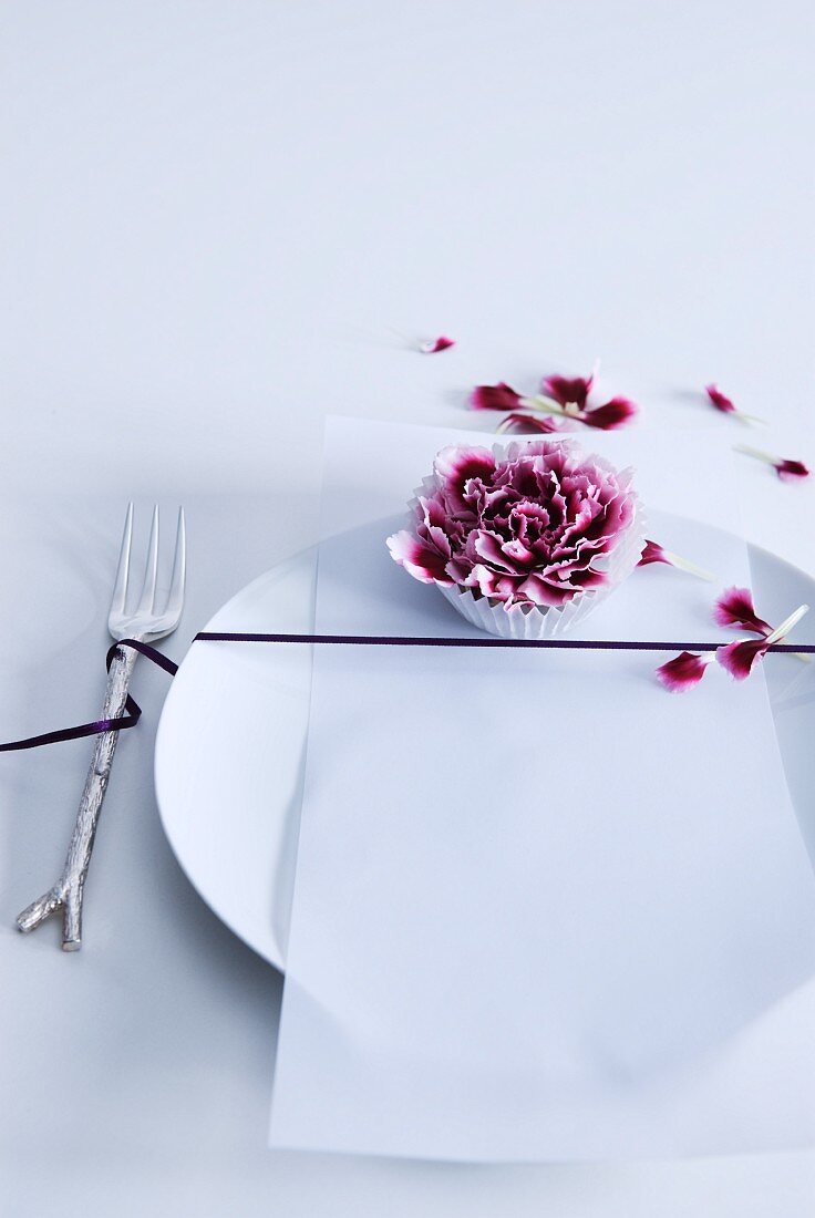 Place setting decorated with black ribbon and purple carnation bloom in paper cake case