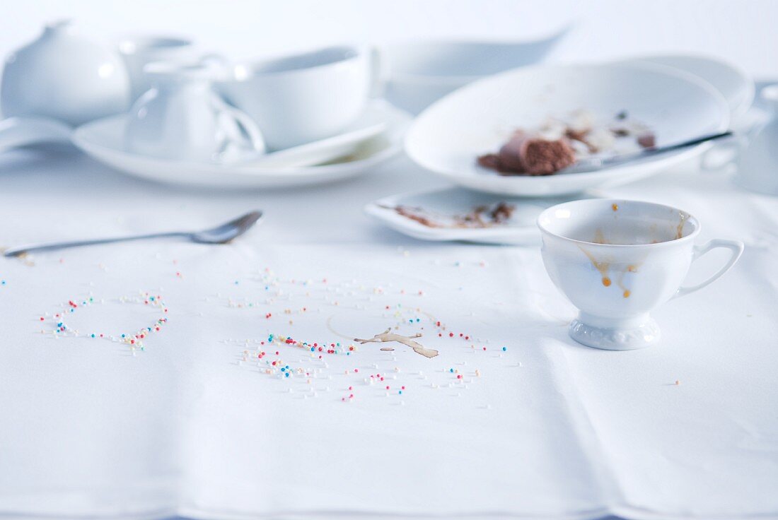 Benutztes weißes Kaffeegeschirr mit bunten Zuckerstreuseln auf weißer Tischdecke