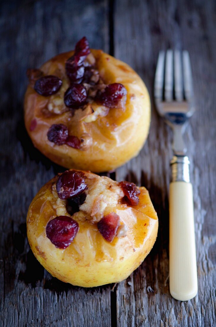 Two baked apples with cranberries on a wooden table with a fork