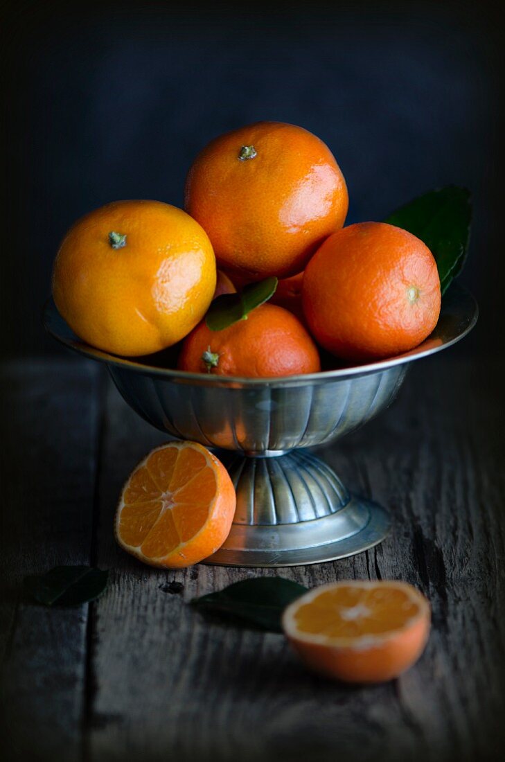 Fresh clementines in a metal bowl on a wooden surface