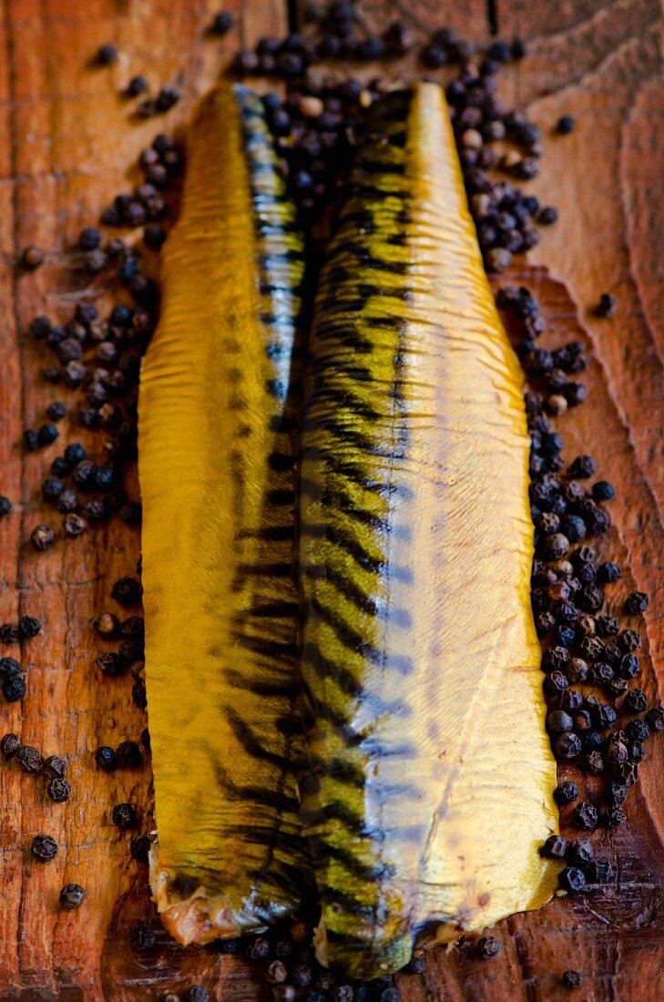 Smoked mackerel fillets on a pine wood board surrounded by peppercorns