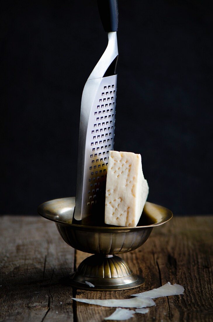 A slice of Pecorino Romano cheese with a greater in a metal bowl