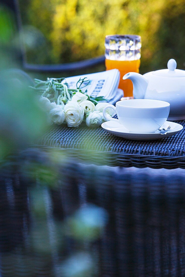 Frühstückstisch mit Tee, weissen Rosen und Zeitung in einem italienischen Garten