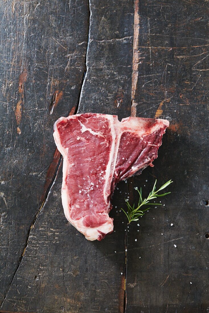 A raw T-bone steak with salt and rosemary