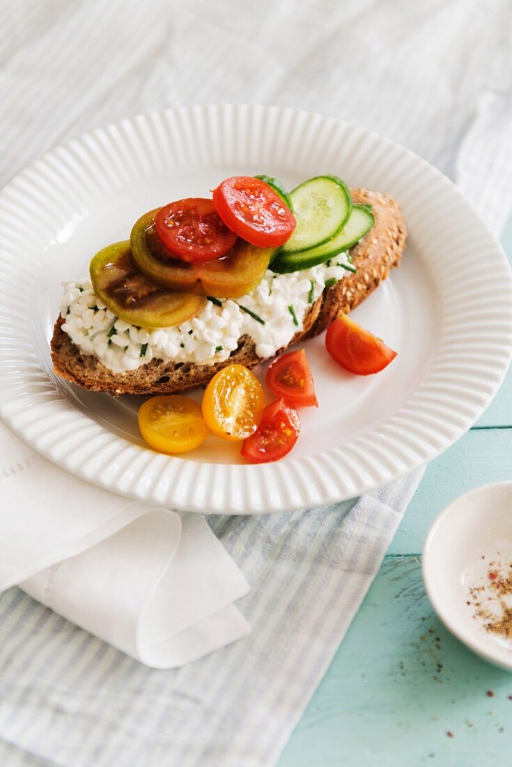 A slice of bread topped with cottage cheese, tomatoes and cucumber