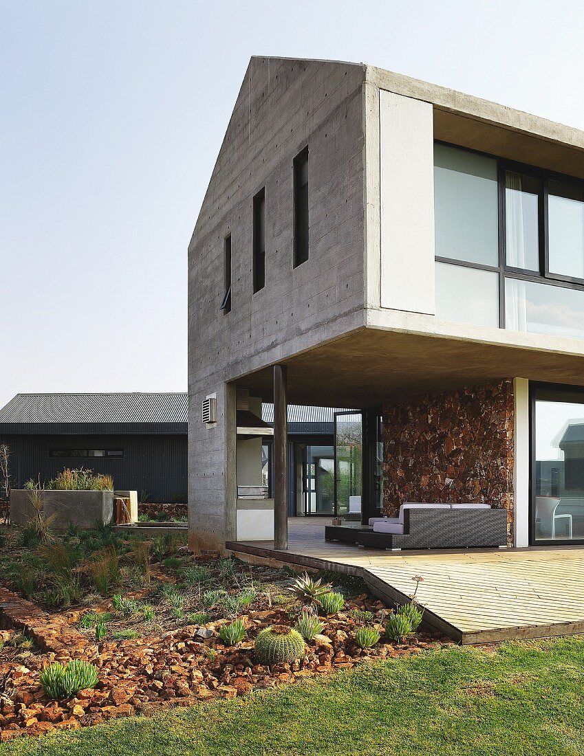 Purist concrete house with roofed terrace on ground floor and bed of cacti and succulents in garden