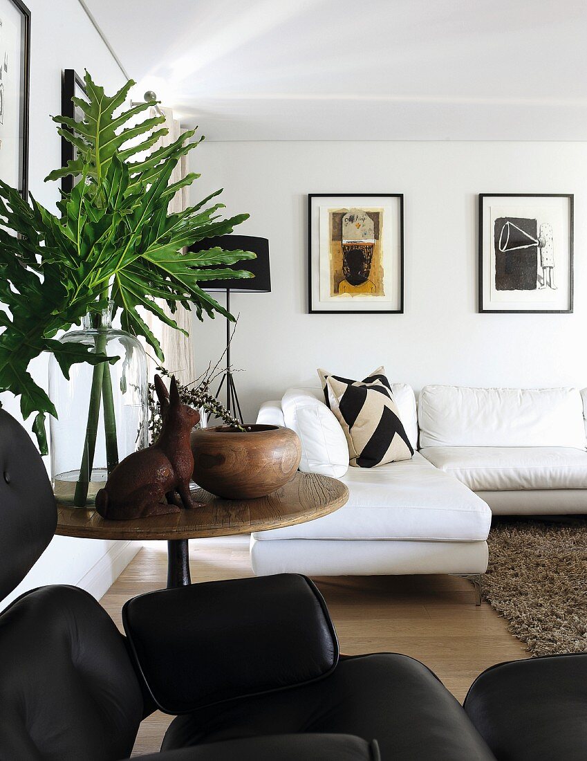 Foliage and rabbit ornament on round wooden side table, modern, white corner sofa and framed pictures in background