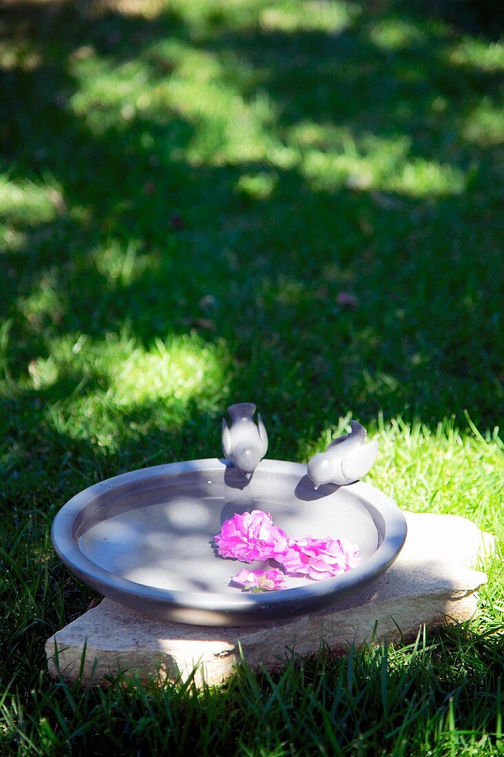 Flowers floating in bird bath with two bird figurines in garden