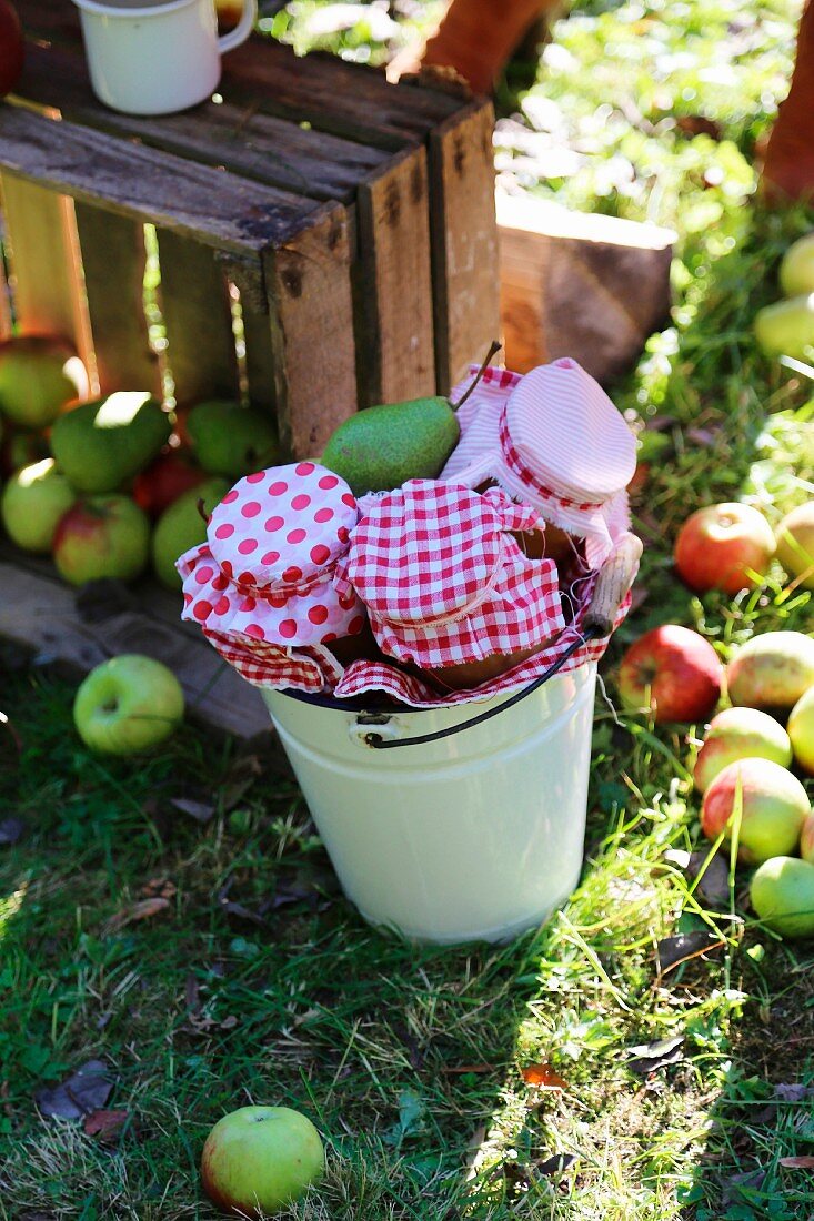 Vintage wooden crate of harvested apples and preserving jars with red and white fabric covers in enamel bucket