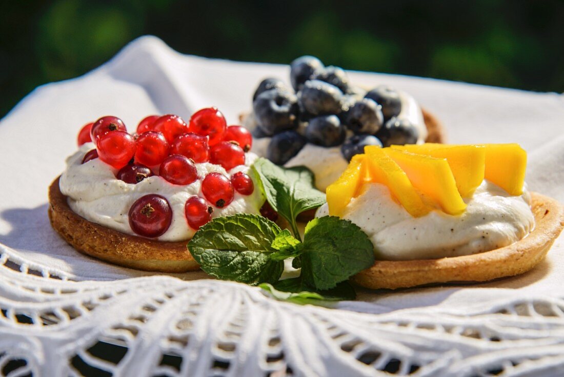 Three fruit tarts with cream, redcurrants, blueberries and mango