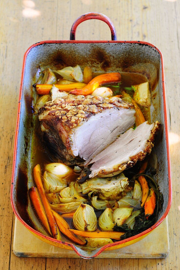 Crispy roast pork with vegetables in a roasting tin
