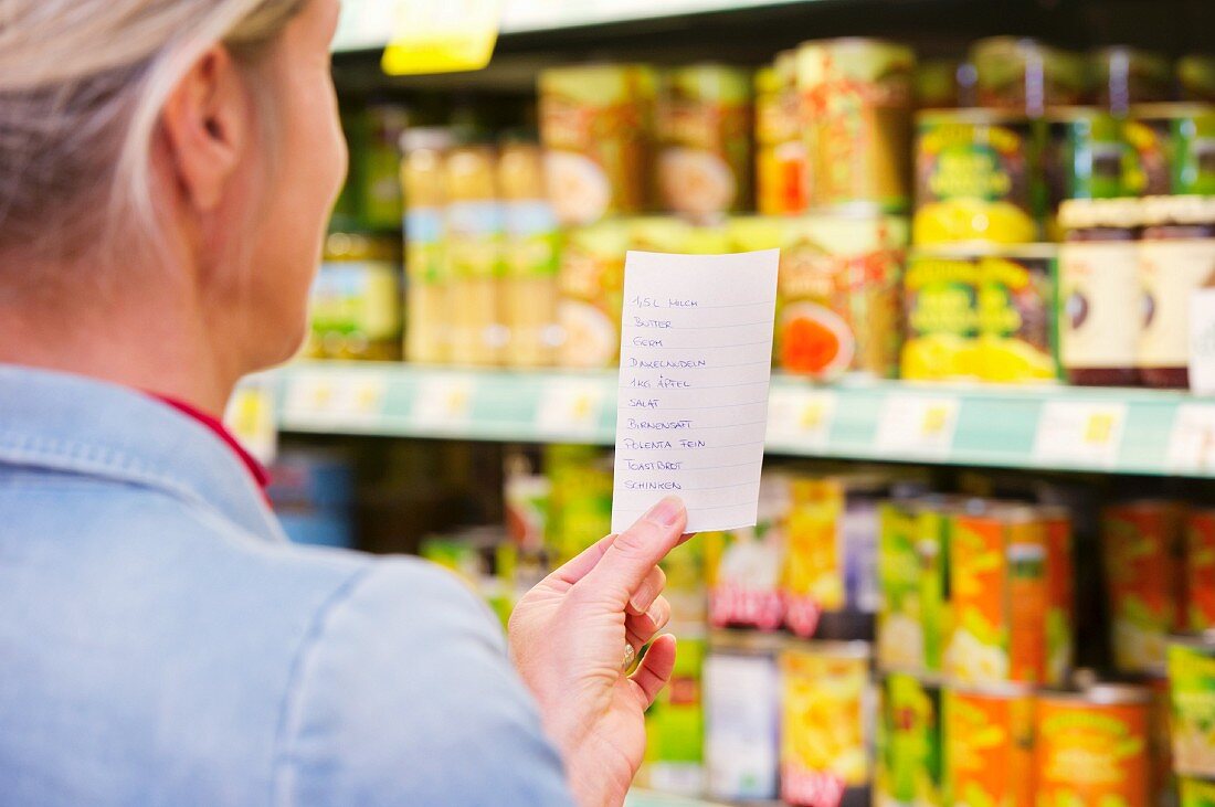 Frau mit Einkaufszettel vor Regal im Lebensmittelgeschäft