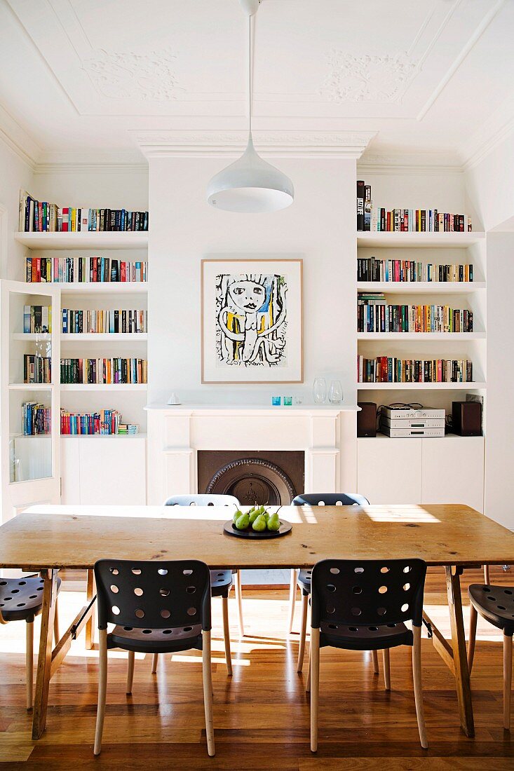 Dining table and designer chairs in front of open fireplace flanked by bookcases in restored interior with stucco ceiling