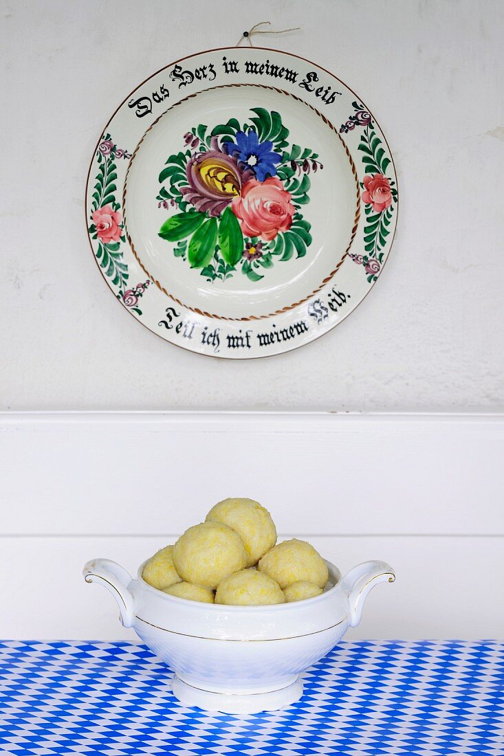 Potato dumplings in a round terrine underneath an old-fashioned painted plate hanging on a wall