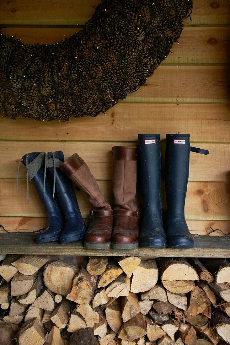 Pairs of boots on board shelf above stacked firewood