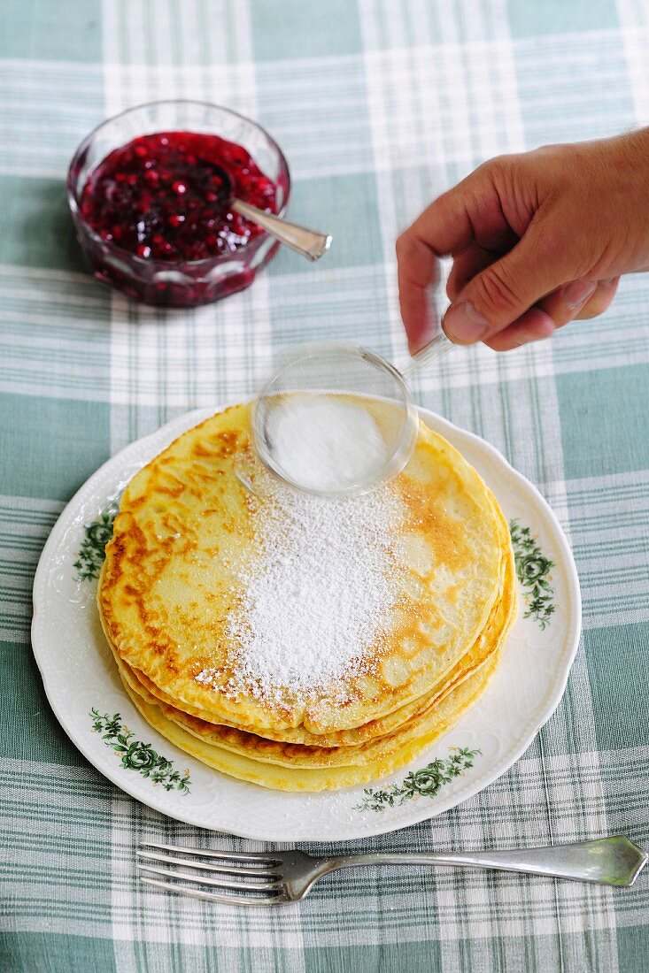 Pancakes being dusted with icing sugar served with jam