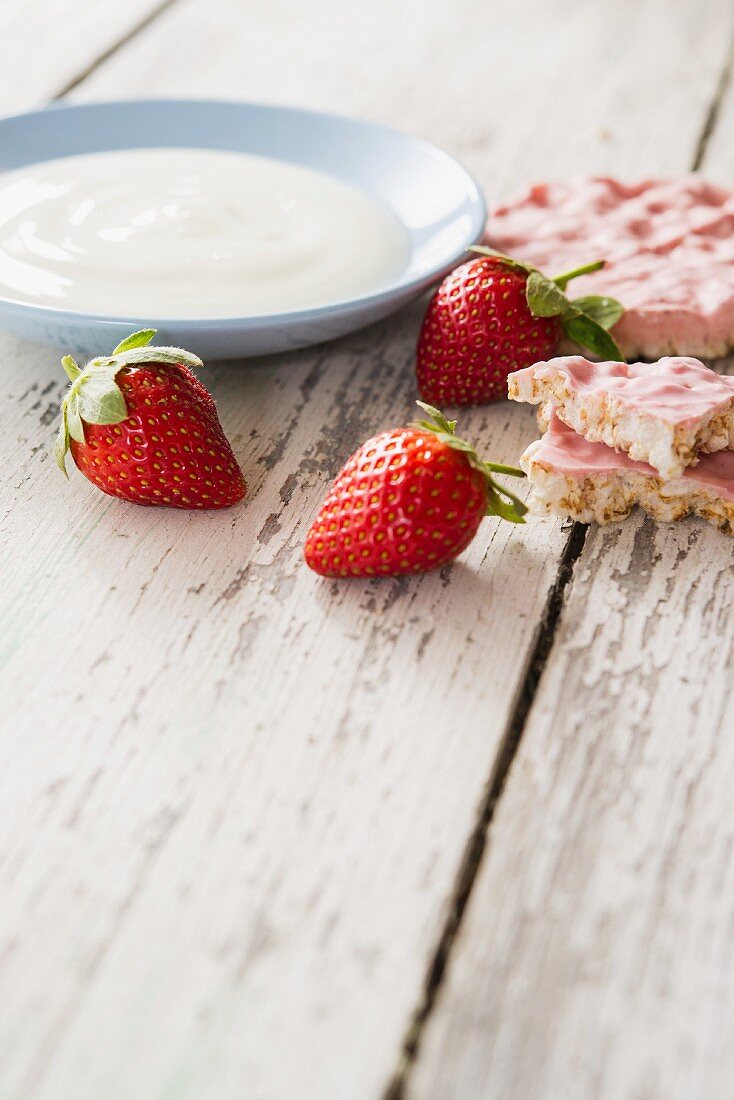 An arrangement featuring a bowl of yogurt, strawberries and strawberry rice crackers