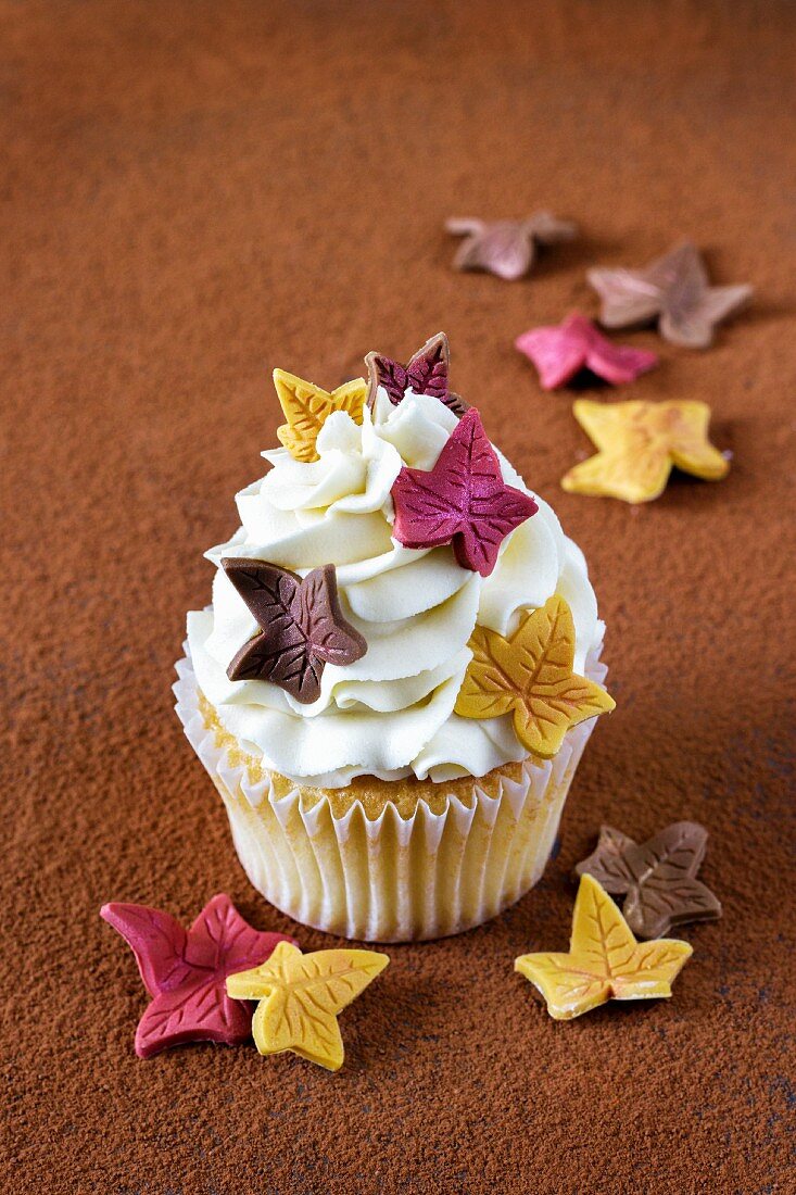 A cinnamon cupcake topped with cream and decorated with sugar leaves