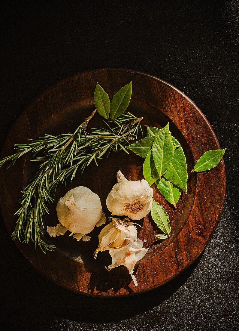 Bay leaves, rosemary and garlic on a wooden plate