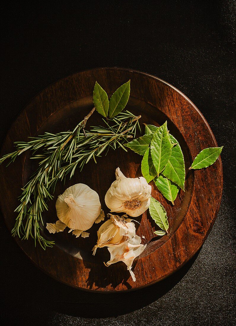 Lorbeerblätter, Rosmarin und Knoblauch auf Holzplatte