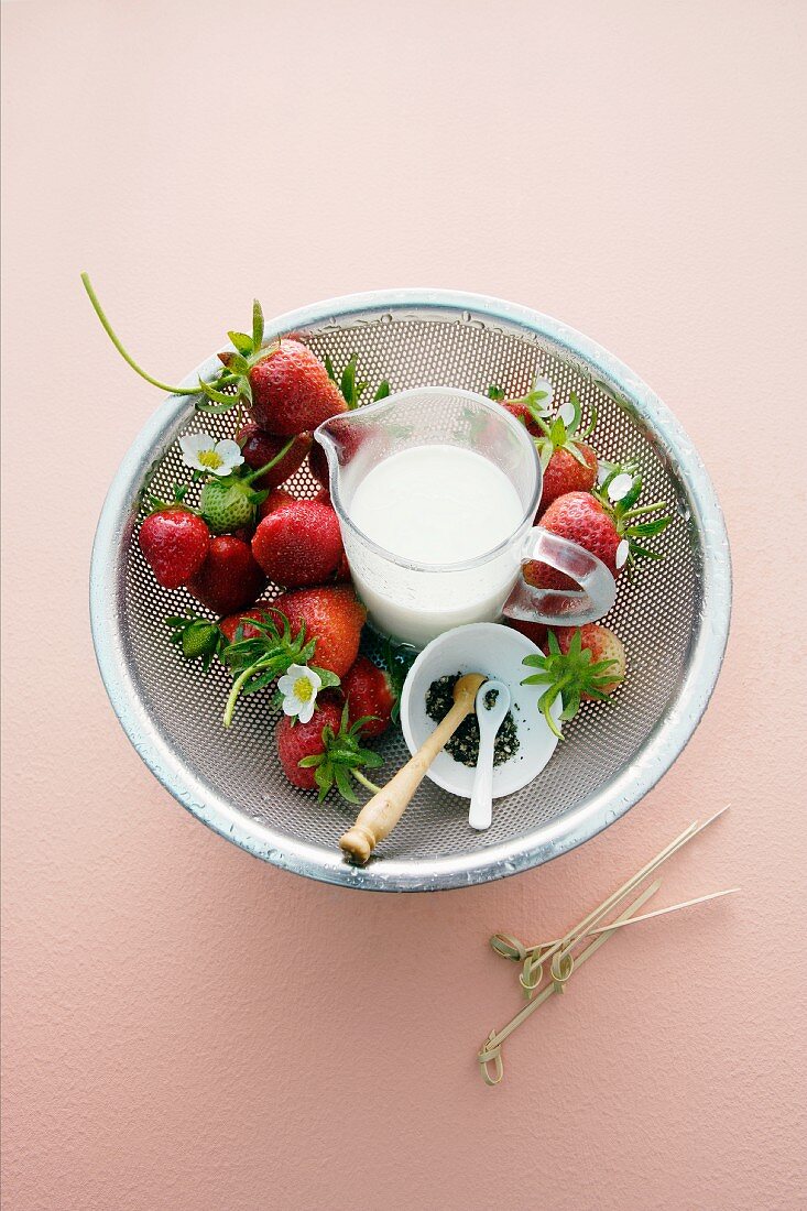 Fresh strawberries and a jug of milk in a colander
