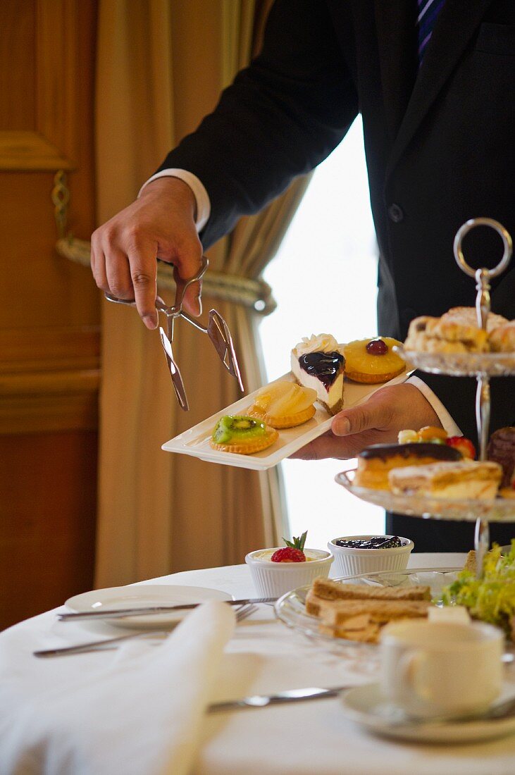 A waiter serving cakes with afternoon tea (England)