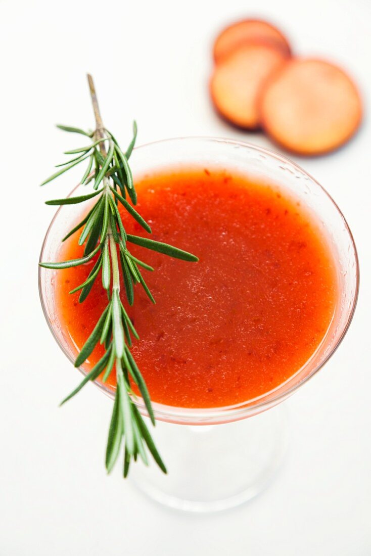 A plum drink garnished with a sprig of rosemary