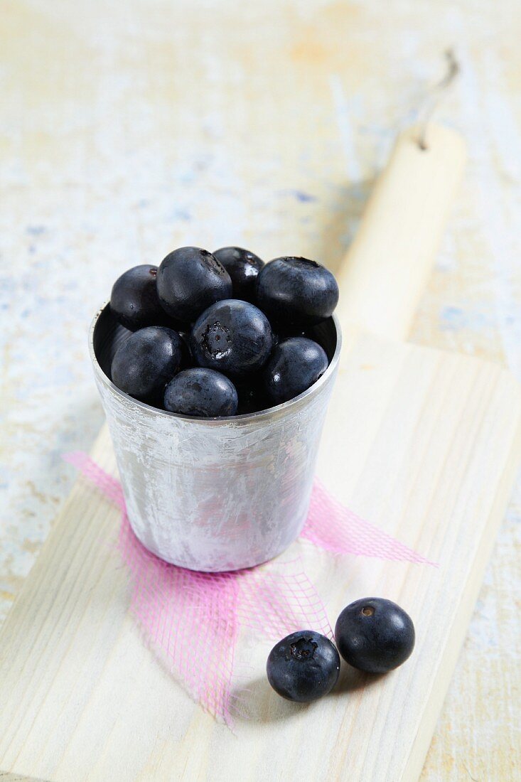 A mug of fresh blueberries on a chopping board