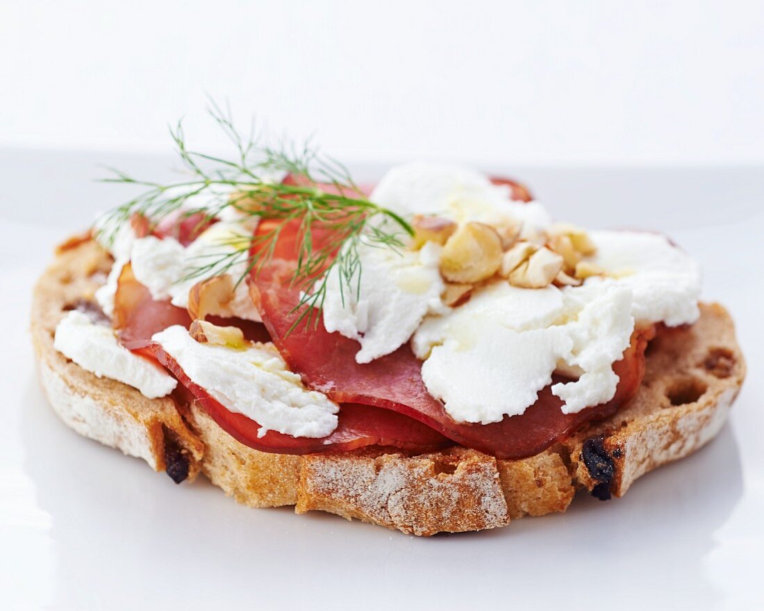 A slice of bread topped with cream cheese, ham and hazelnuts